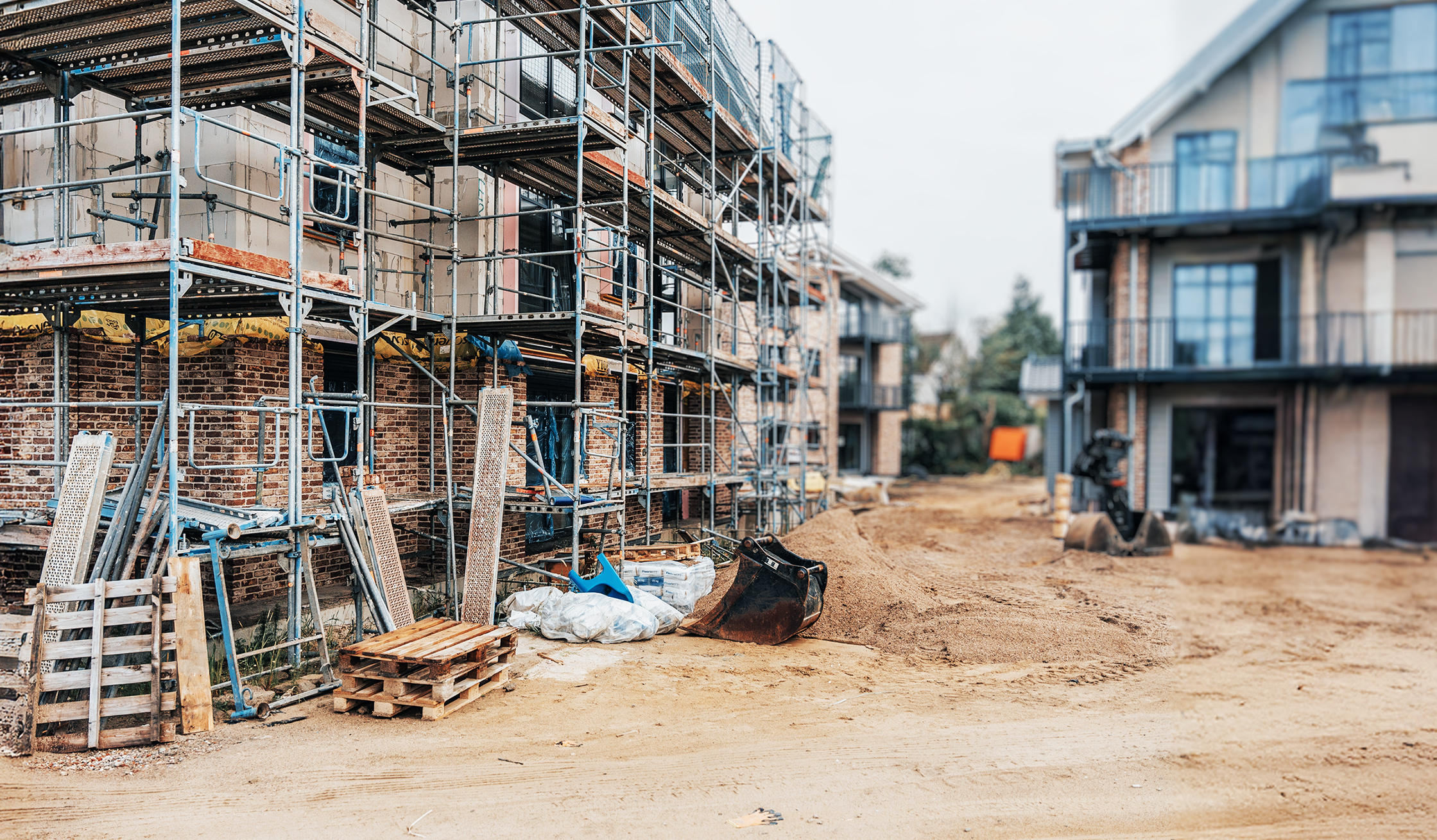Referenz Mehrfamilienhäuser Büsum Johannsenallee: Ein unfertiges Wohnhaus, von Baugerüsten umgeben. Davor liegen Erdhaufen und Baumaterialien.