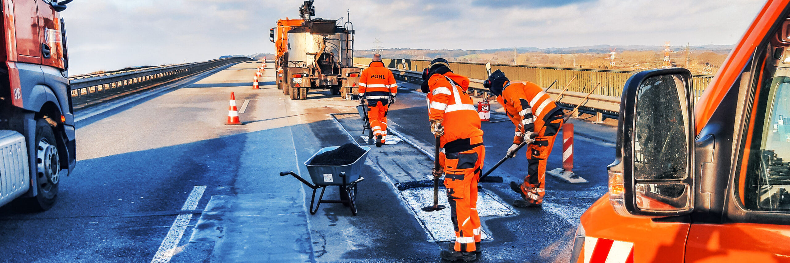 Mitarbeitende von POHL reparieren die Fahrbahn auf einer Brücke, umgeben von Absperrkegeln.