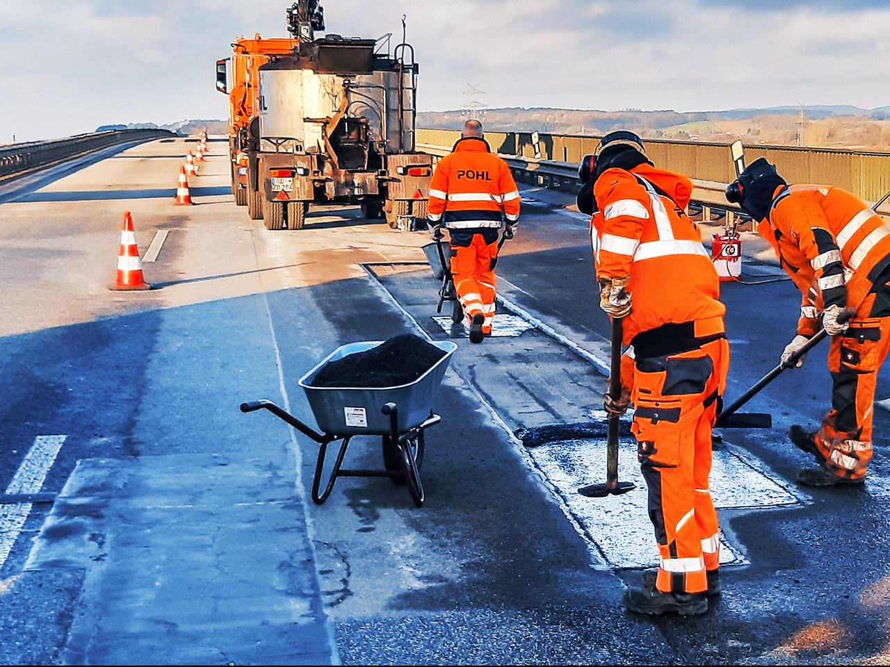 Mitarbeitende von POHL reparieren die Fahrbahn auf einer Brücke, umgeben von Absperrkegeln.