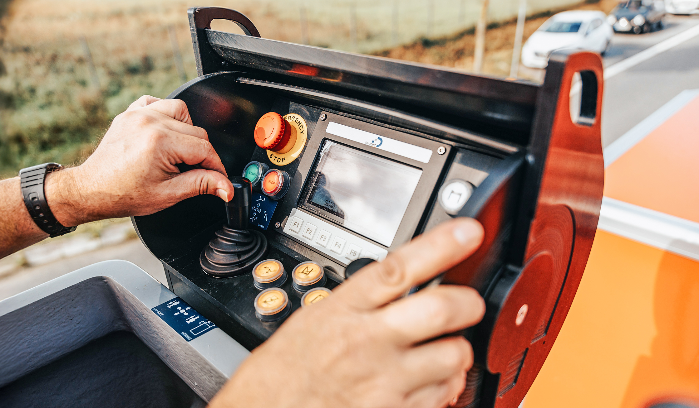 Referenz Wartung Straßenbeleuchtung Büdelsdorf: Vorne hält eine Hand das Bedienfeld am POHL-Fahrzeug mit Hebel, Tasten und kleinem Bildschirm. Hinten verläuft der Straßenrand unscharf.