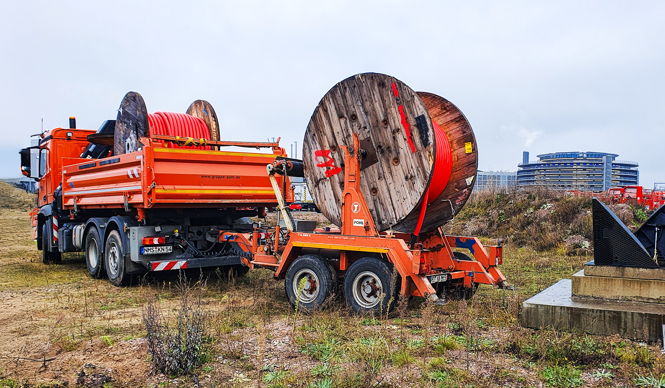 Referenz Stromversorgung Hamburg Flughafen: Ein schwerer Lastwagen von POHL fährt über eine grüne Wiese. Auf seinem Anhänger liegen zwei riesige Kabeltrommeln.