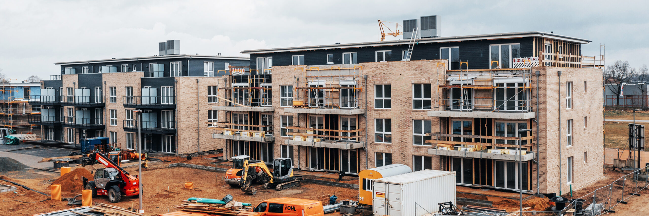 Referenz Mehrfamilienhäuser Neumünster: Blick von erhöhter Position auf eine große Baustelle mit mehreren neuen Häusern, Baugeräten und orangefarbenen Containern der Firma POHL.
