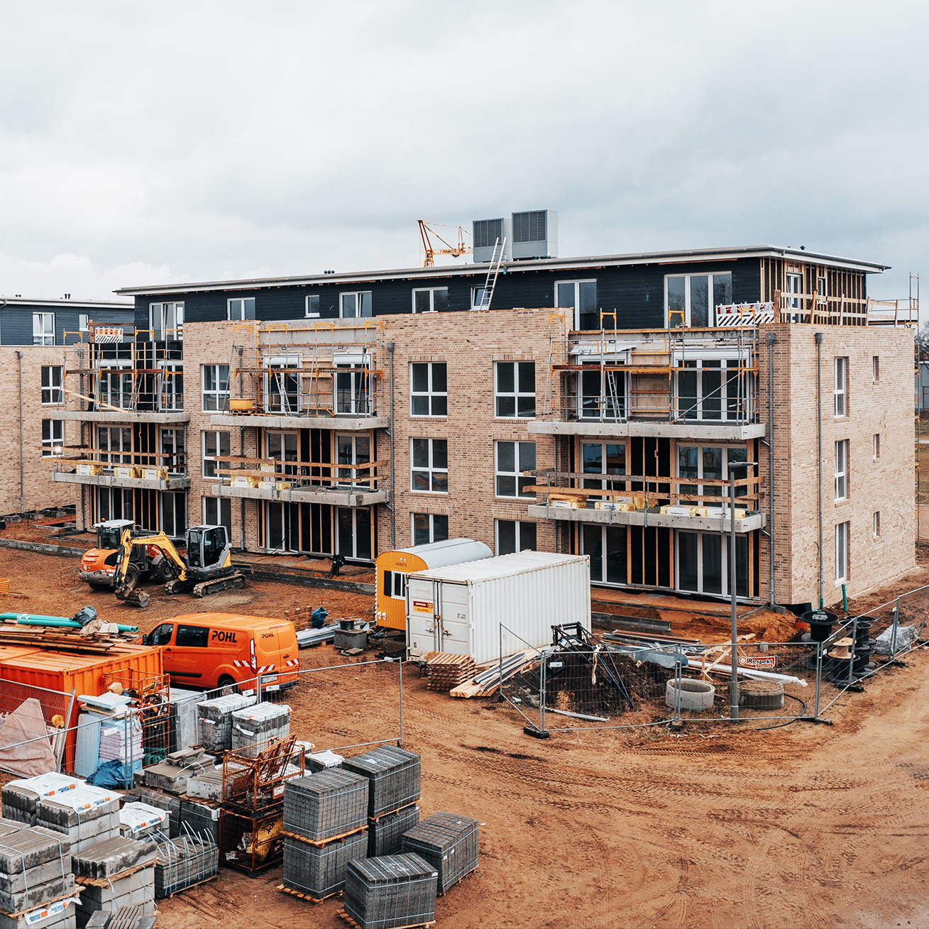 Referenz Mehrfamilienhäuser Neumünster: Blick von erhöhter Position auf eine große Baustelle mit mehreren neuen Häusern, Baugeräten und orangefarbenen Containern der Firma POHL.