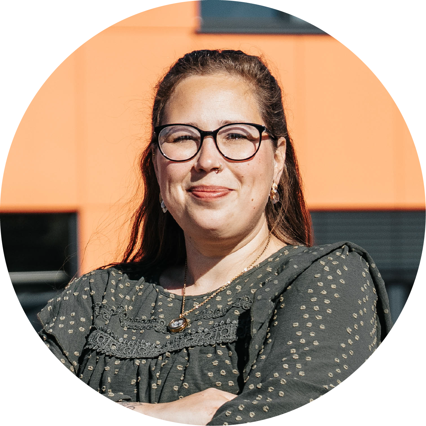 Porträt von Isabell Deutel, weibliche Person mit Brille und dunkler Kleidung vor orangem Hintergrund.