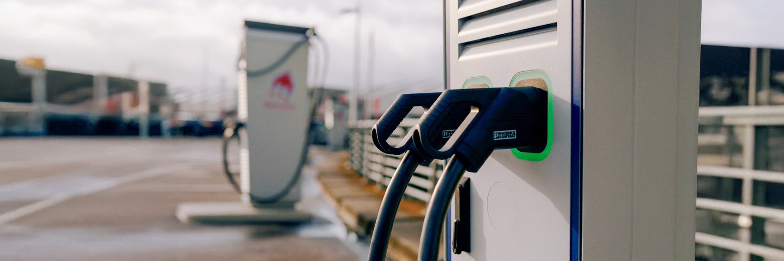 Nahaufnahme einer modernen Ladesäule mit zwei angeschlossenen schwarzen Ladekabeln für Elektrofahrzeuge.