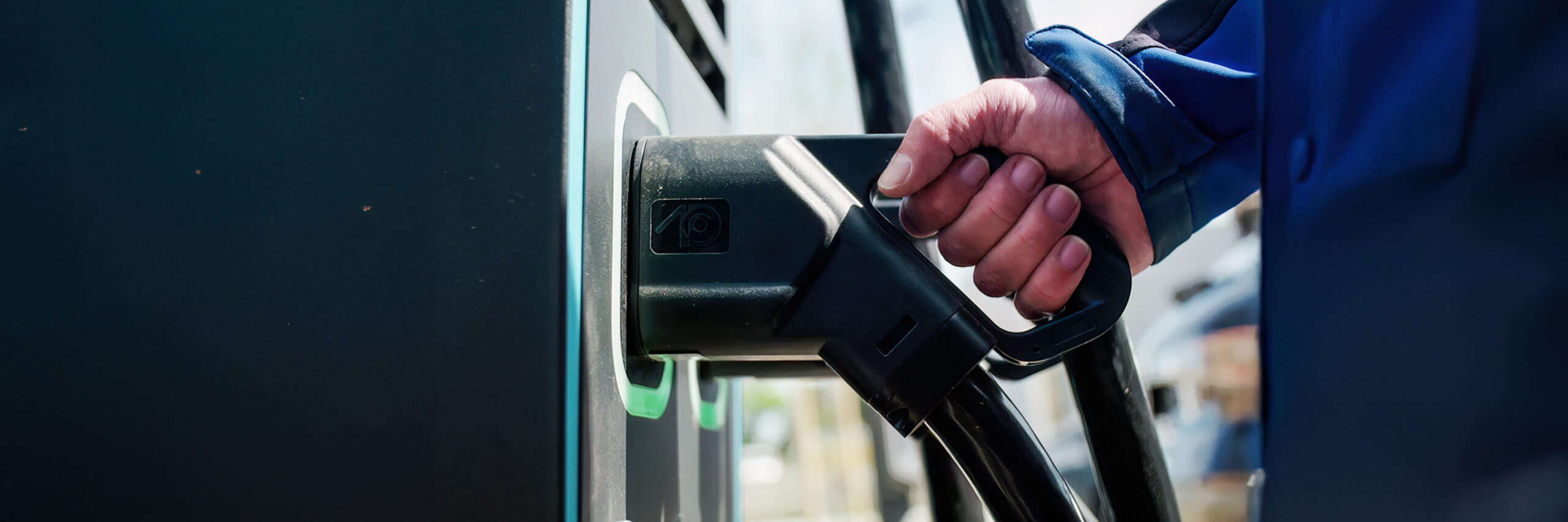 Hand steckt ein Ladekabel in die Steckdose einer Elektroladestation für ein Elektroauto.