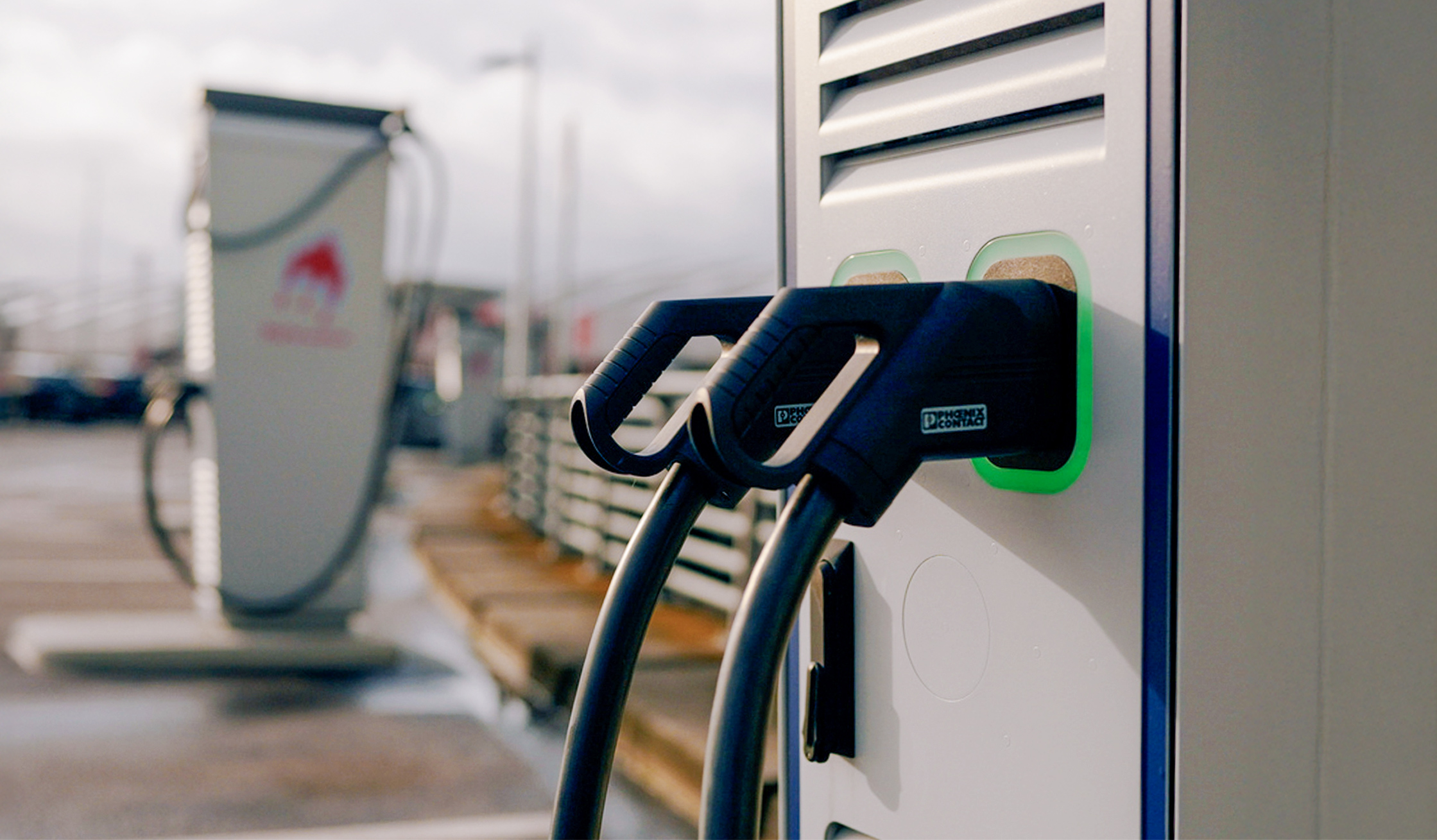 Nahaufnahme einer modernen Ladesäule mit zwei angeschlossenen schwarzen Ladekabeln für Elektrofahrzeuge.