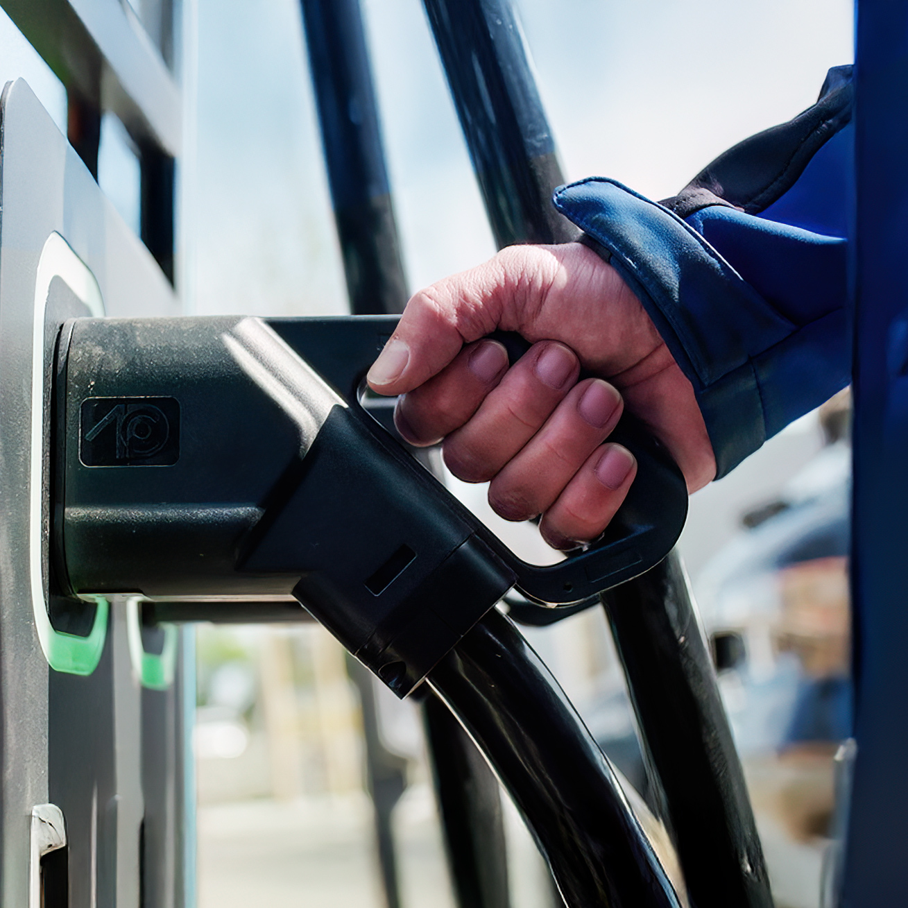 Hand steckt ein Ladekabel in die Steckdose einer Elektroladestation für ein Elektroauto.