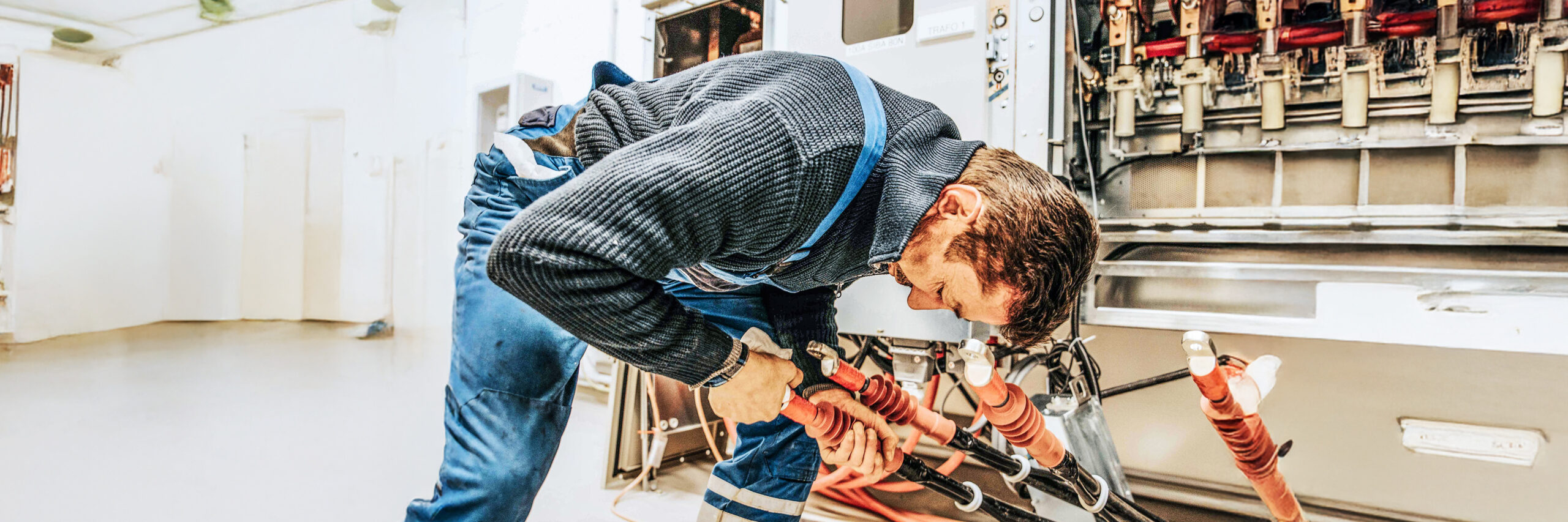 Ein POHL Monteur in blauer Arbeitskleidung installiert dicke Kabel in einem Technikraum.
