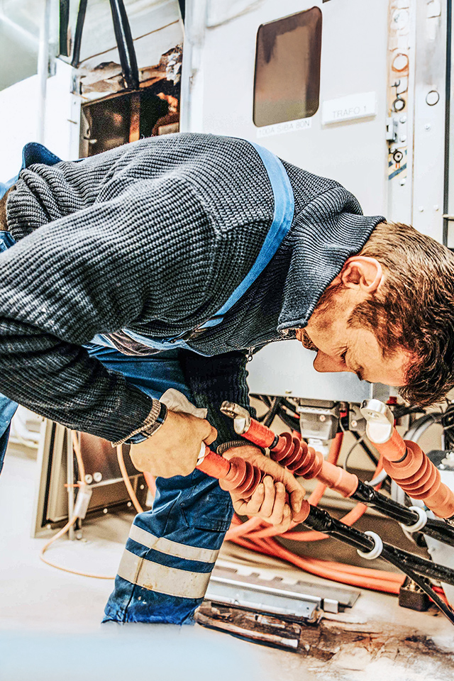 Ein POHL Monteur in blauer Arbeitskleidung installiert dicke Kabel in einem Technikraum.