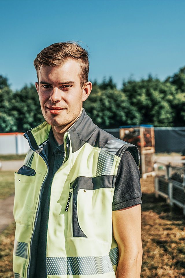 Auf einem Eventgelände steht ein POHL-Mitarbeiter in heller Warnweste vor einem weißen Zelt und Materialkisten; Hintergrund unscharf.