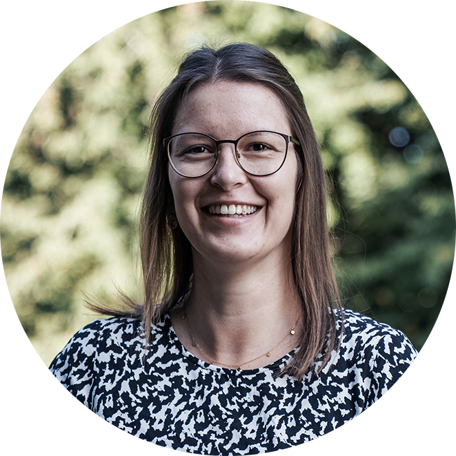 Portrait einer lächelnden Frau mit Brille und schulterlangen Haaren vor unscharfem, grünem Hintergrund.