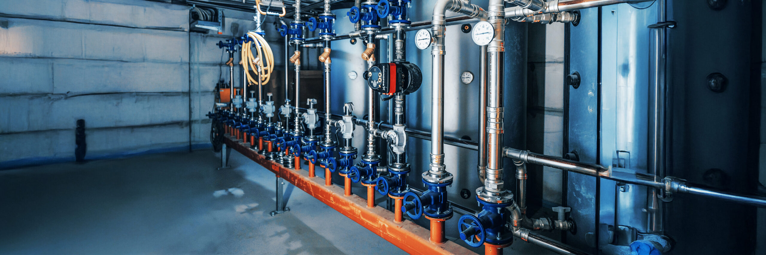 Technikraum mit Rohren, Ventilen und Messgeräten für die Gebäudetechnik.