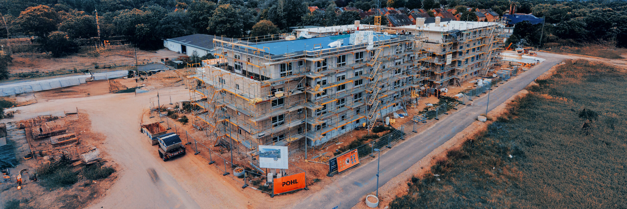 Großer Wohnkomplex im Bau mit Baugerüsten und Kran, Baustellenschilder und Geräte von POHL.