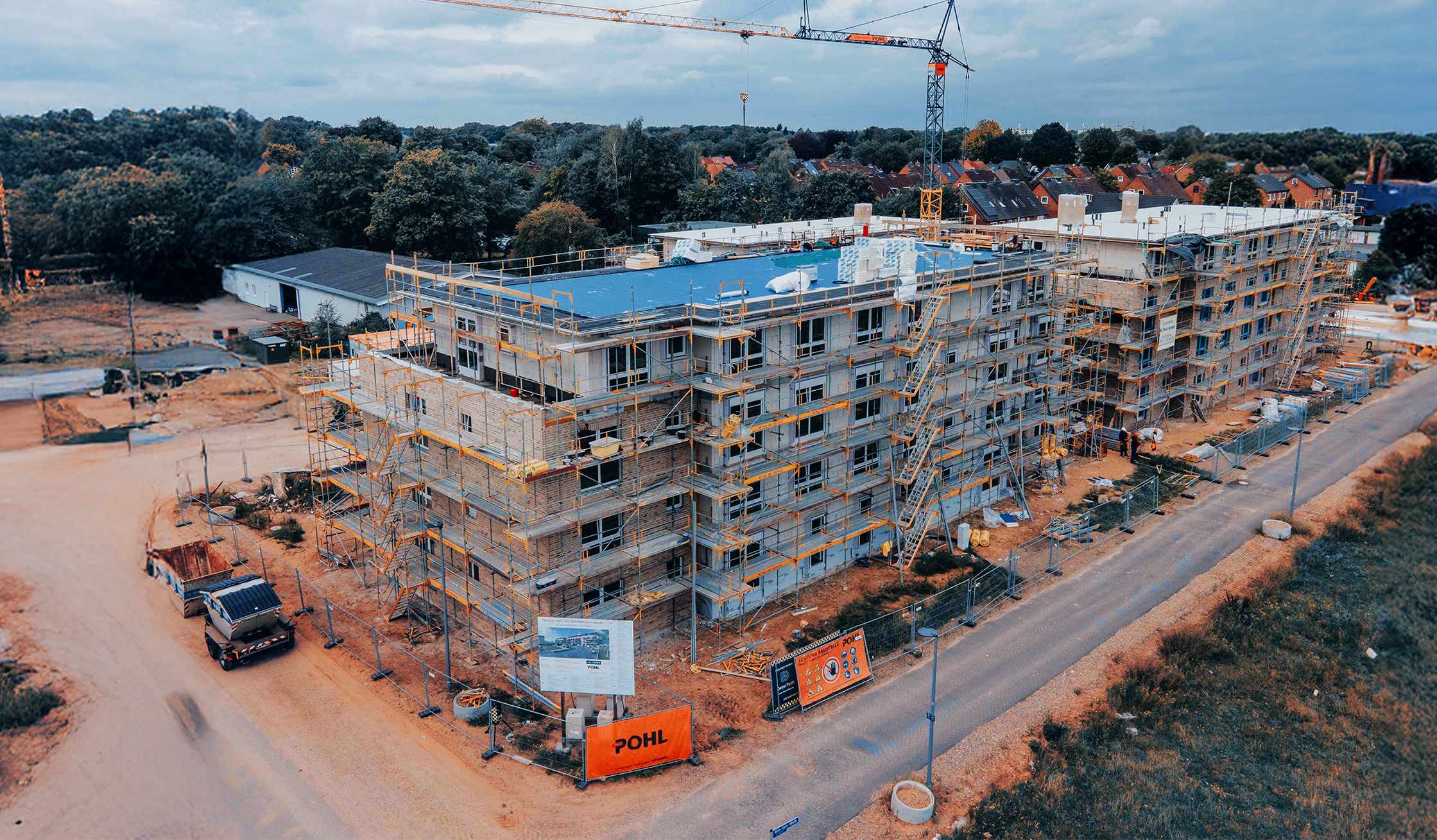 Großer Wohnkomplex im Bau mit Baugerüsten und Kran, Baustellenschilder und Geräte von POHL.