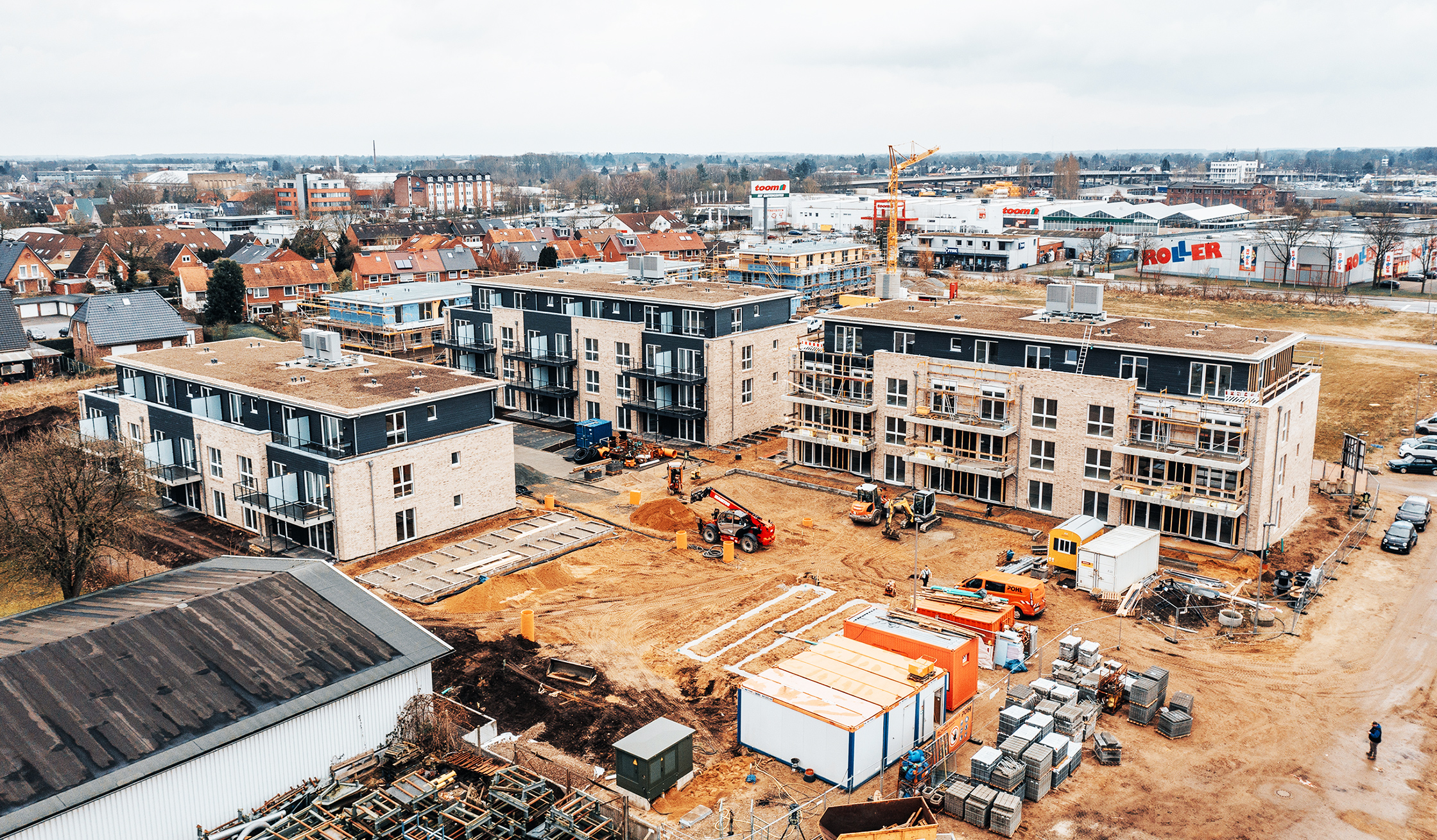 Referenz Mehrfamilienhäuser Neumünster: Luftaufnahme einer großen Baustelle mit mehreren Neubauten, Baukran und Containern der Firma POHL