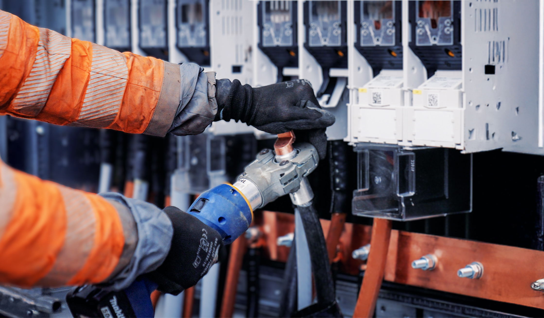 Nahaufnahme von Händen in schwarzen Handschuhen, die mit einem Spezialwerkzeug dicke Kabel an einem Schaltschrank bearbeiten. Die Person trägt eine orangene Pohl-Schutzjacke.