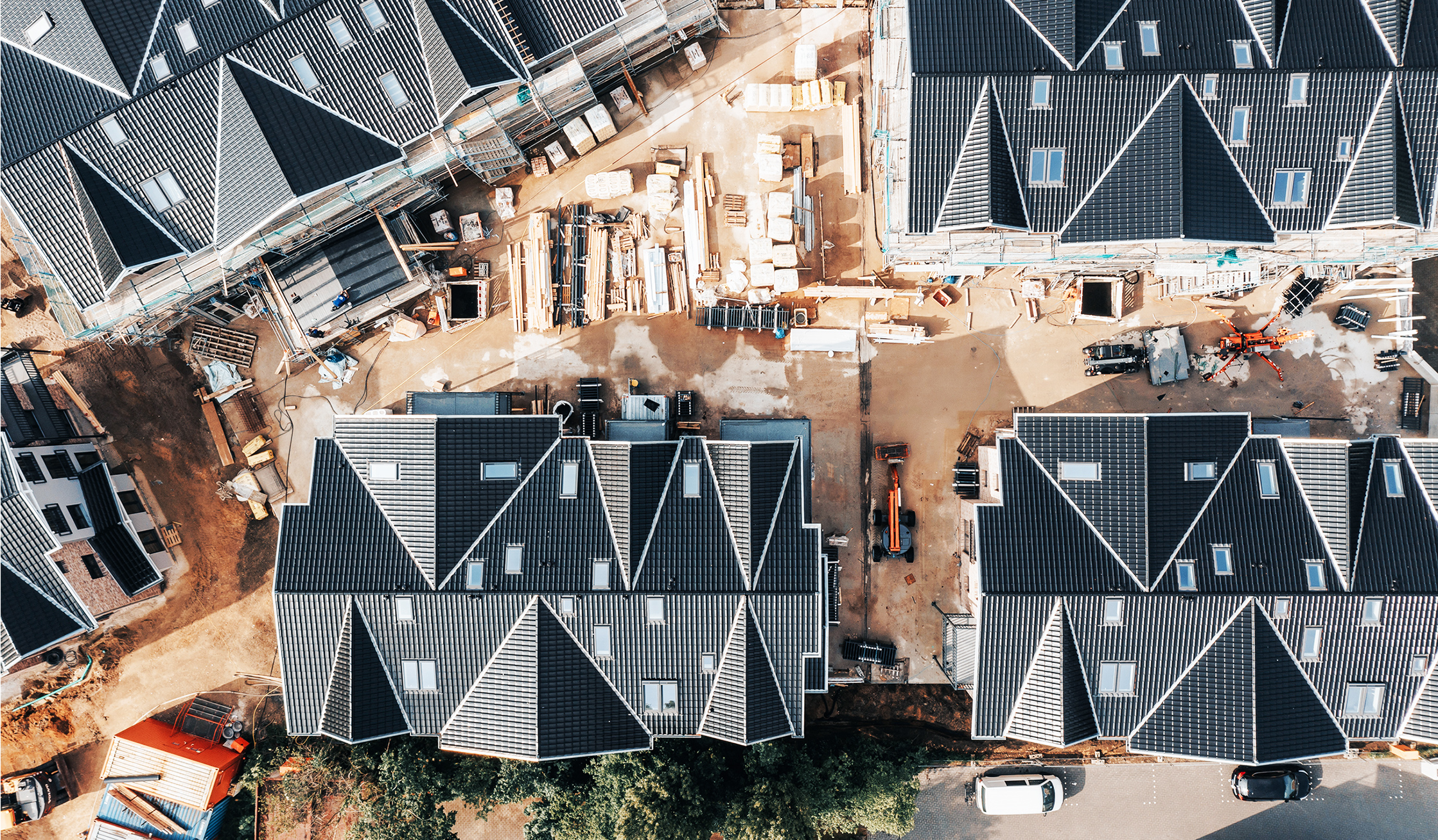 Referenz Mehrfamilienhäuser Büsum Johannsenallee: Blick senkrecht von oben auf eine Baustelle mit eng stehenden Häusern, dunklen Dächern und Baumaterialien zwischen den Gebäuden.