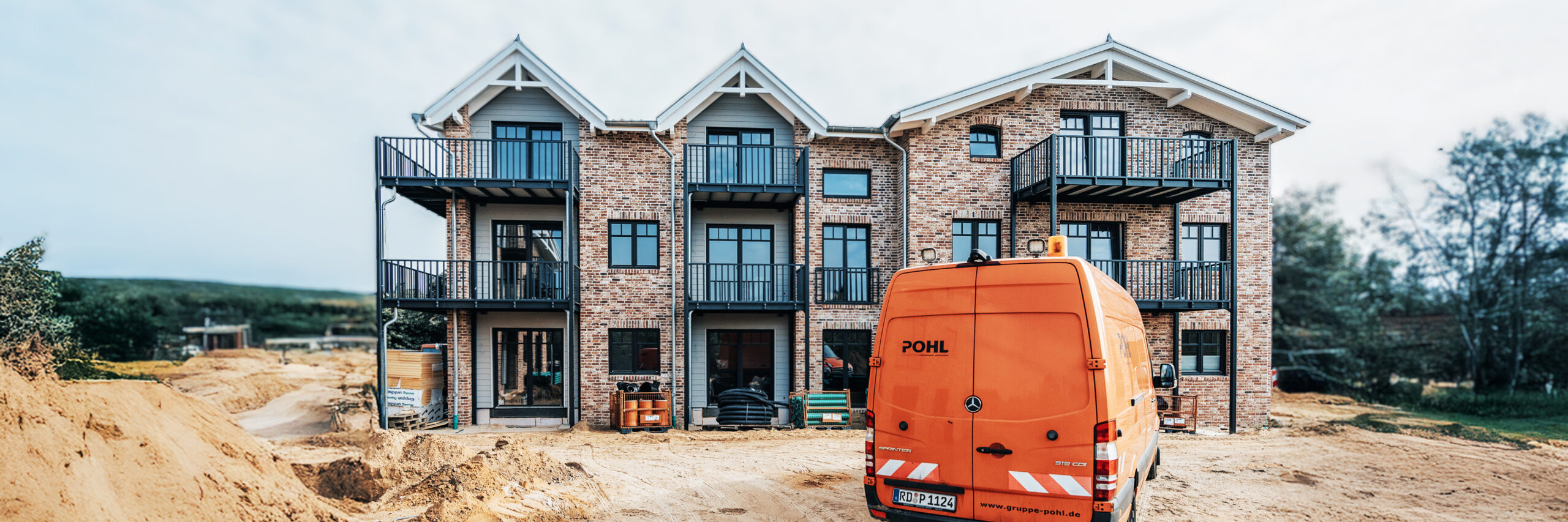 Referenz Mehrfamilienhäuser Büsum Johannsenallee: Backstein-Mehrfamilienhaus mit Firmenfahrzeug der Firma Pohl davor.