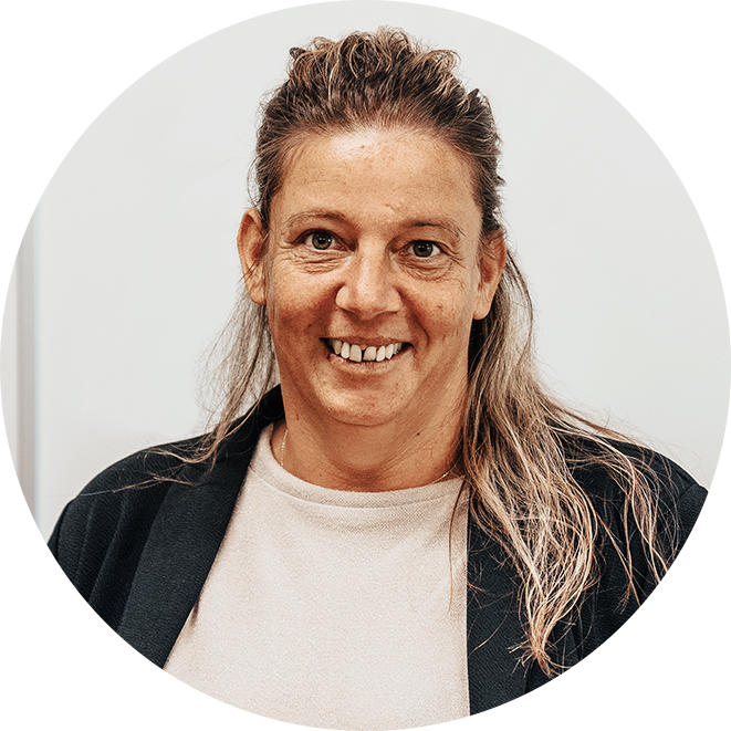 Ein Porträit einer weiblich gelesenen Person. Sie hat blonde lange Haare die halb hoch zusammengesteckt sind und lächelt freundlich in die Kamera. Sie trägt ein weißes T-Shirt und einen schwarzen Cardigan.