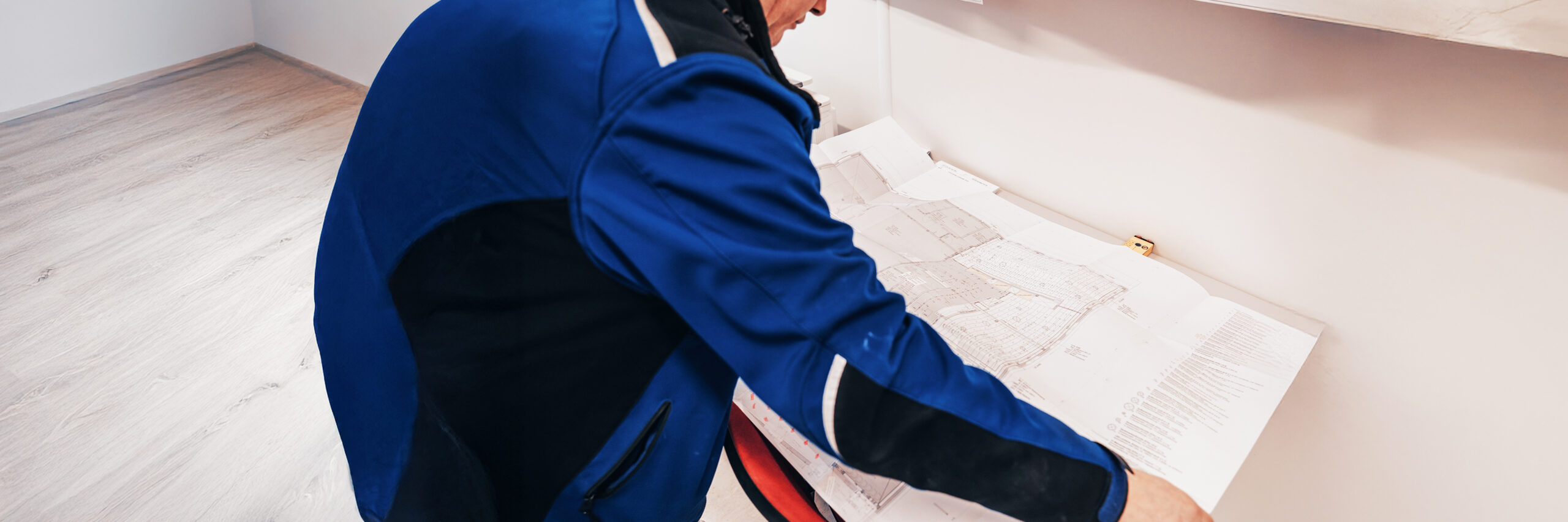 Person in blauer Jacke betrachtet großformatige Baupläne.