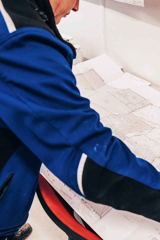 Person in blauer Jacke betrachtet großformatige Baupläne.