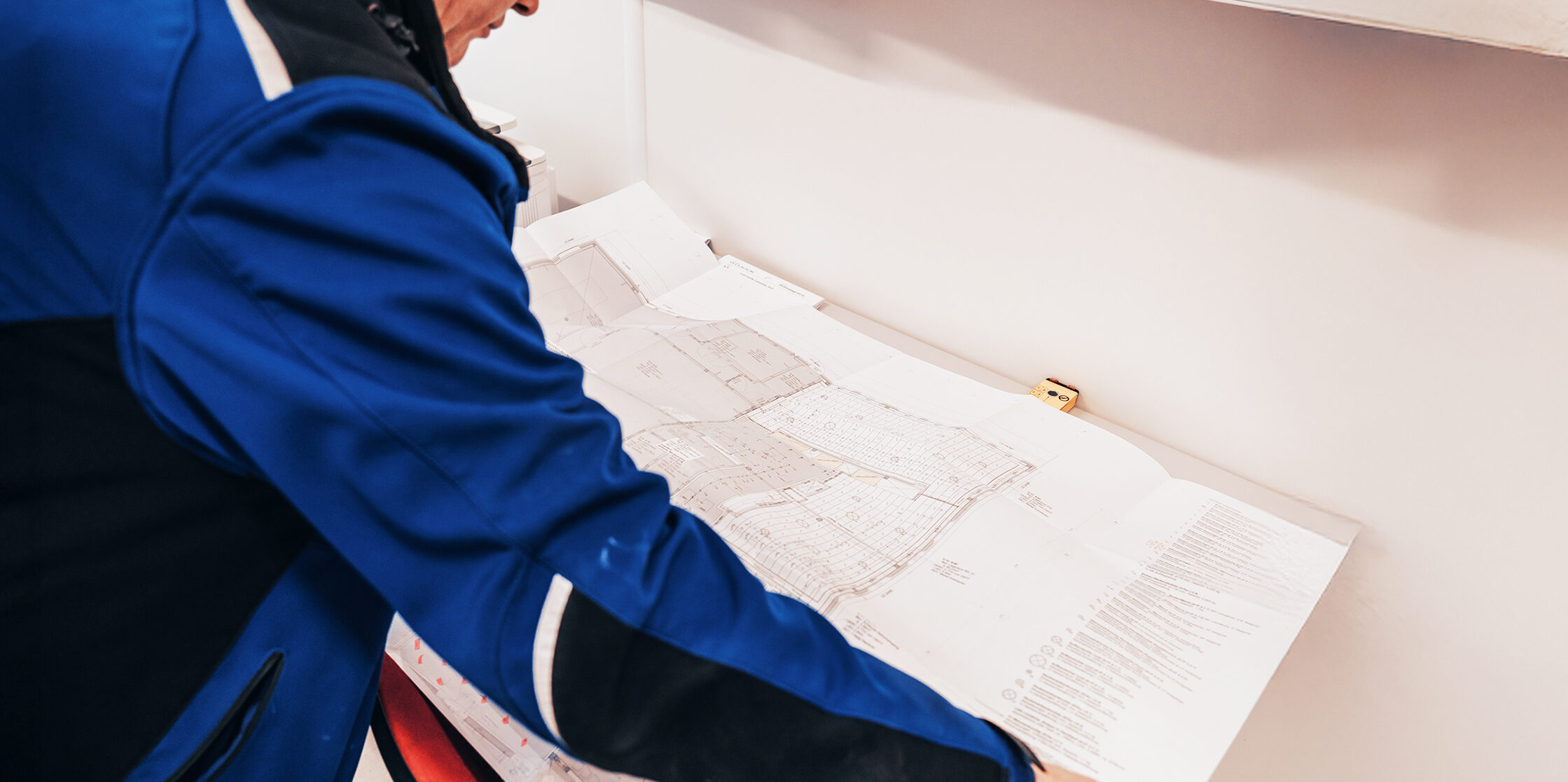 Person in blauer Jacke betrachtet großformatige Baupläne.