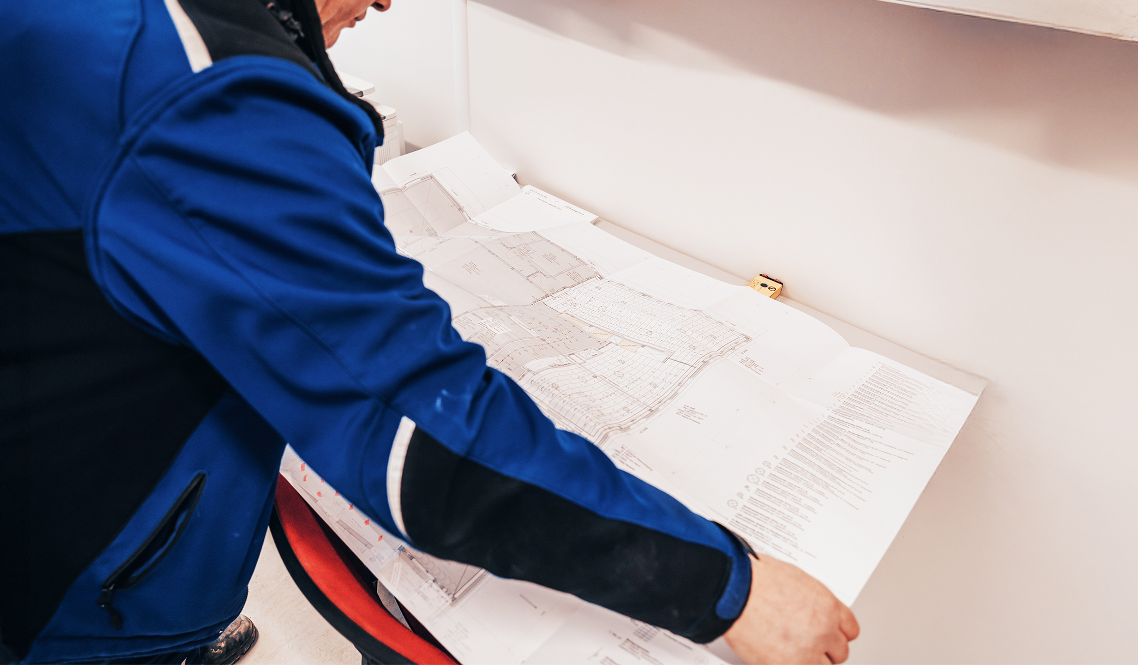 Person in blauer Jacke betrachtet großformatige Baupläne.