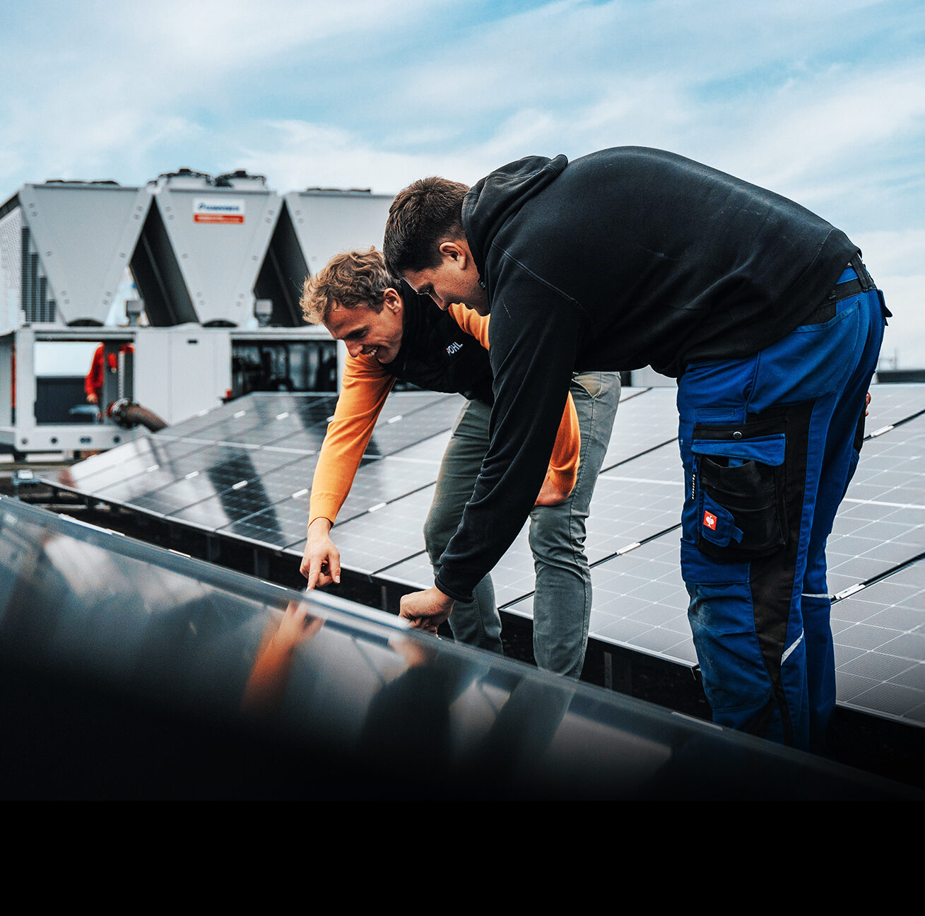 Zwei Männer prüfen ein Solarpanel auf einem Dach mit technischer Anlage.