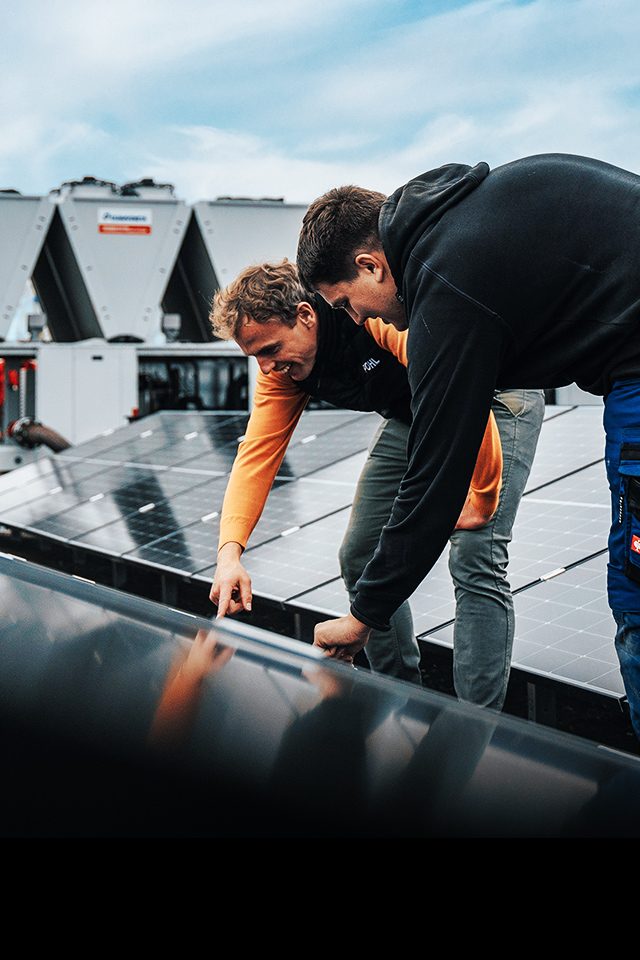 Zwei Männer prüfen ein Solarpanel auf einem Dach mit technischer Anlage.