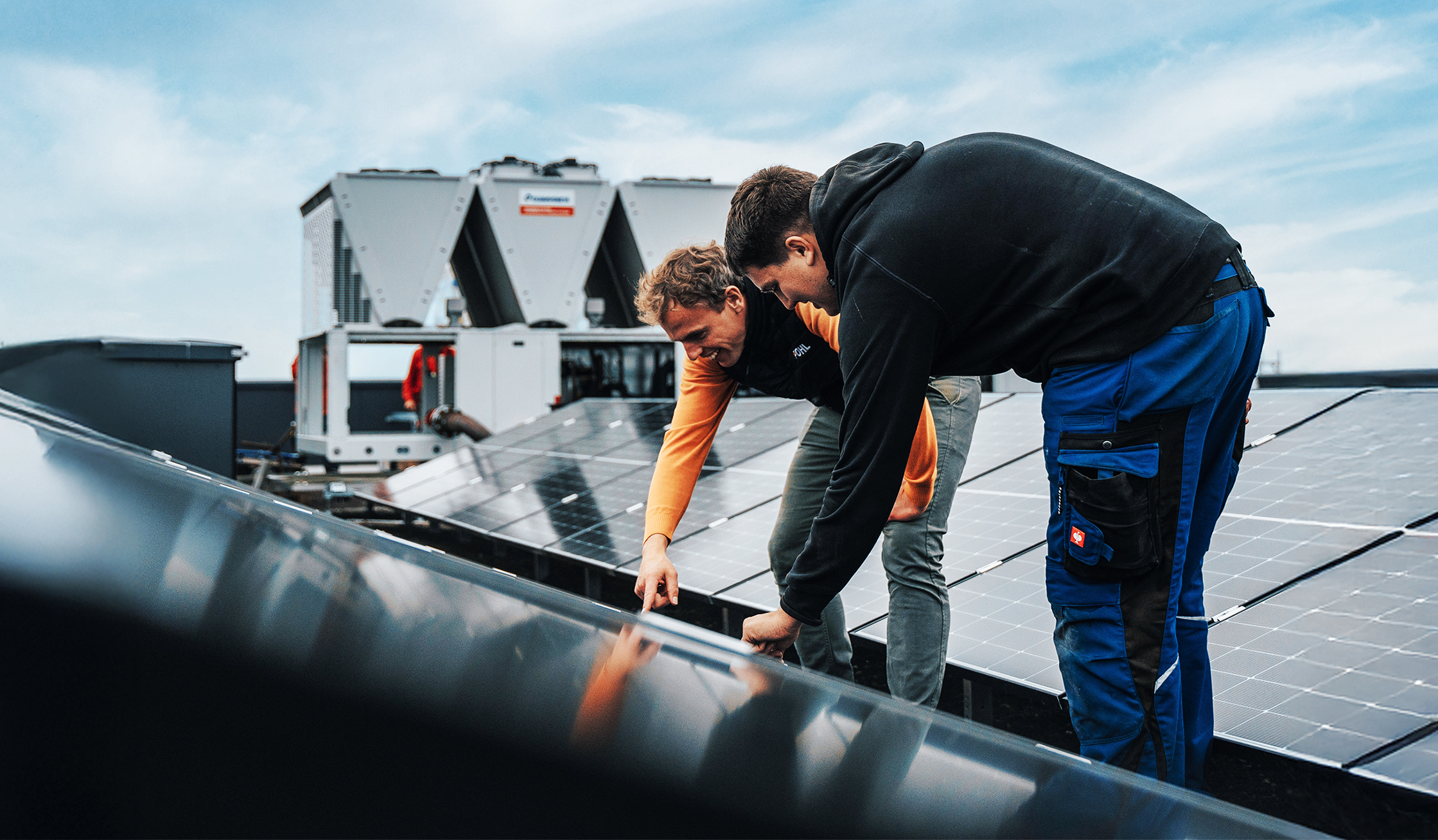 Zwei Männer prüfen ein Solarpanel auf einem Dach mit technischer Anlage.