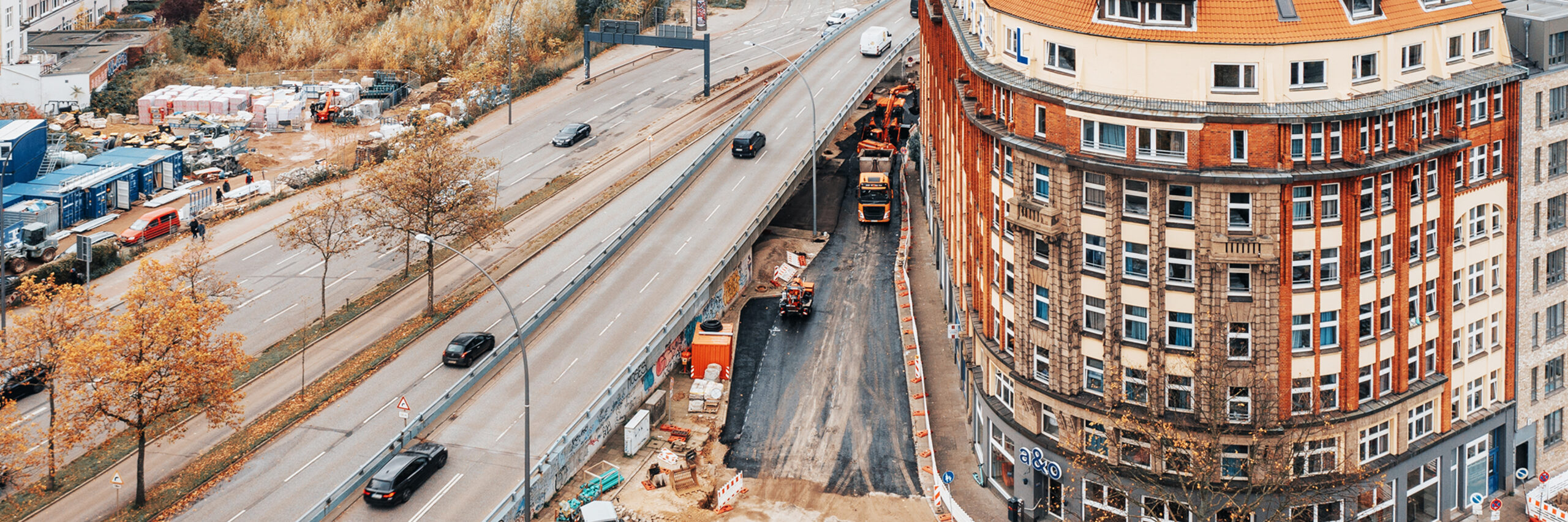 Verkehrsinfrastruktur: Referenz Umbau Hamburg Högerdamm: Baustelle vor runder Häuserfront, die Baustelle ist abgesperrt, Fahrzeuge von POHL auf der Baustelle.