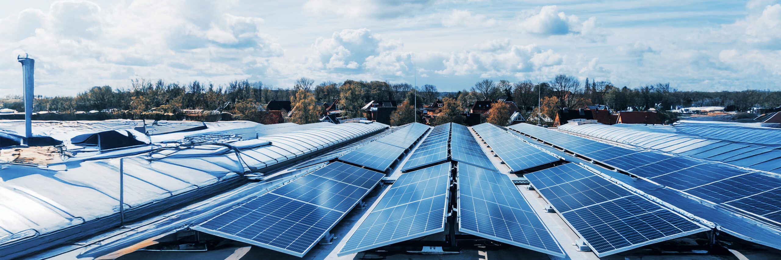 Solaranlage auf einem Dach, im Hintergrund eine Siedlung mit Bäumen.
