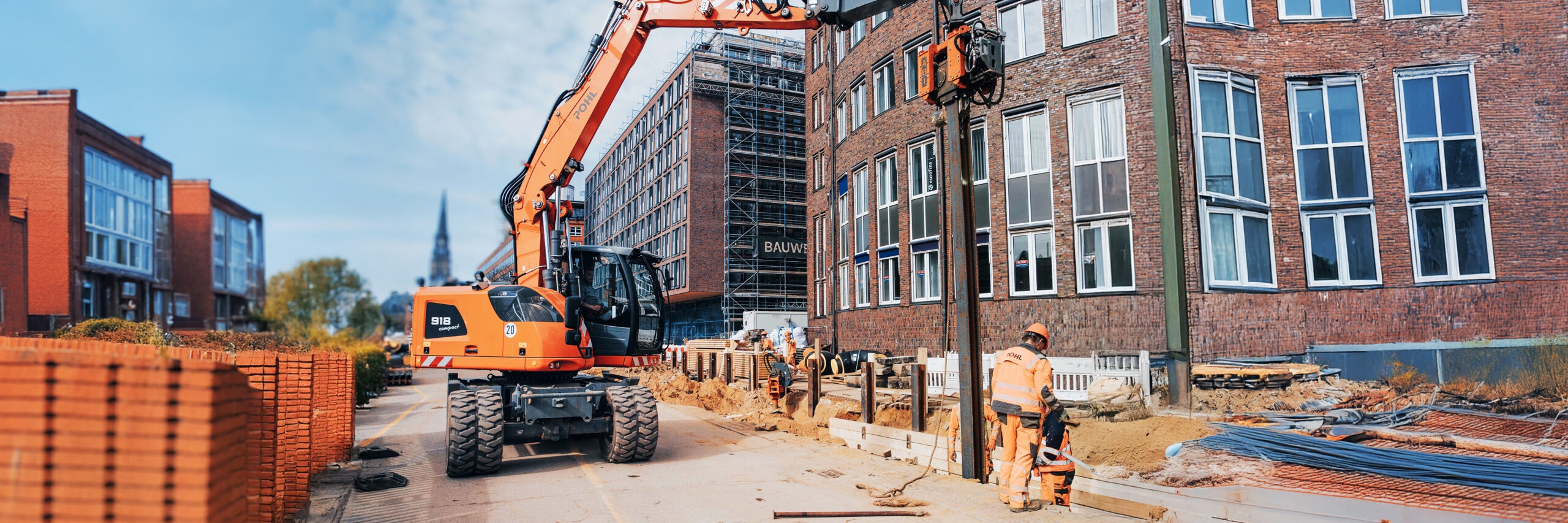 Bagger von POHL auf einer städtischen Baustelle, Mitarbeitende von POHL arbeiten am Gehwegrand.