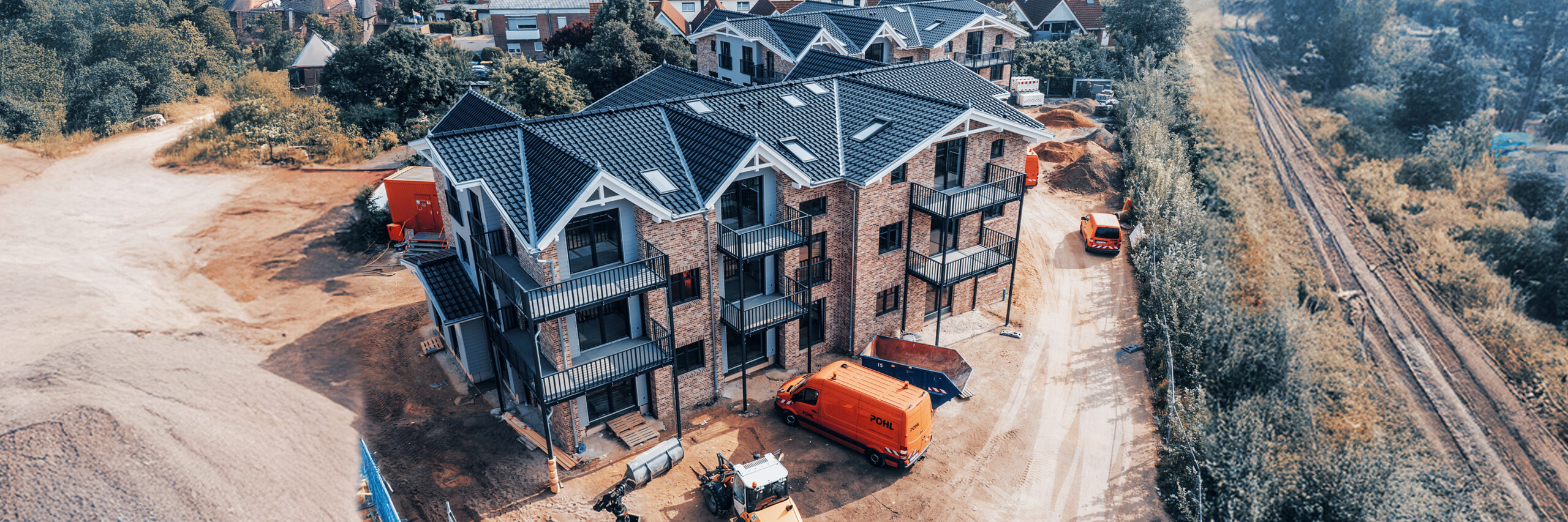 Mehrfamilienhaus im Bau mit Ziegelfassade, davor Fahrzeuge und Maschinen von POHL.