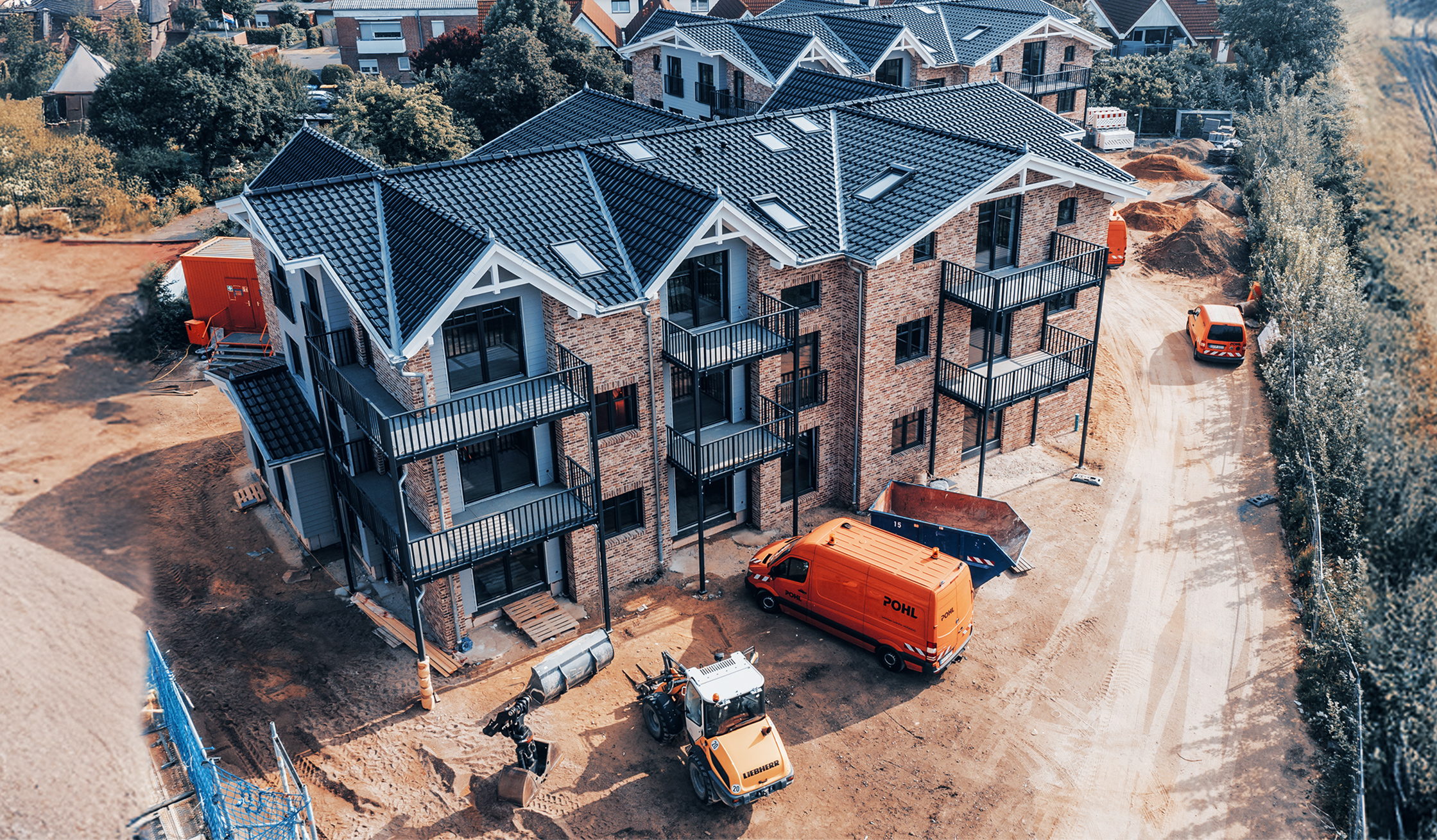 Mehrfamilienhaus im Bau mit Ziegelfassade, davor Fahrzeuge und Maschinen von POHL.