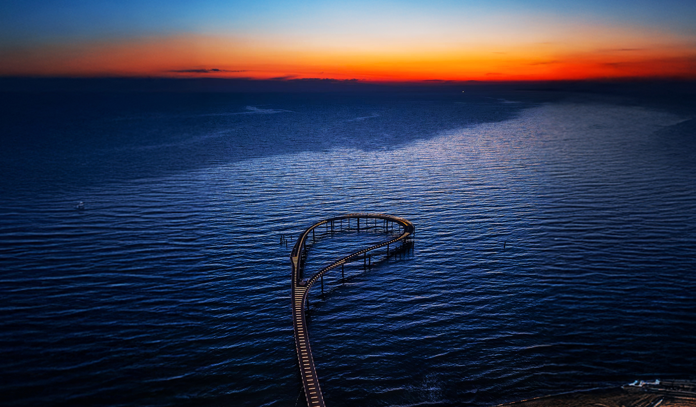 Referenz Maritim Seebrücke Timmendorfer Strand: Unten in der Mitte führt eine geschwungene Seebrücke über das dunkle Wasser in Richtung Horizont. Oben am Horizont liegt ein schmaler, heller Streifen Himmel.