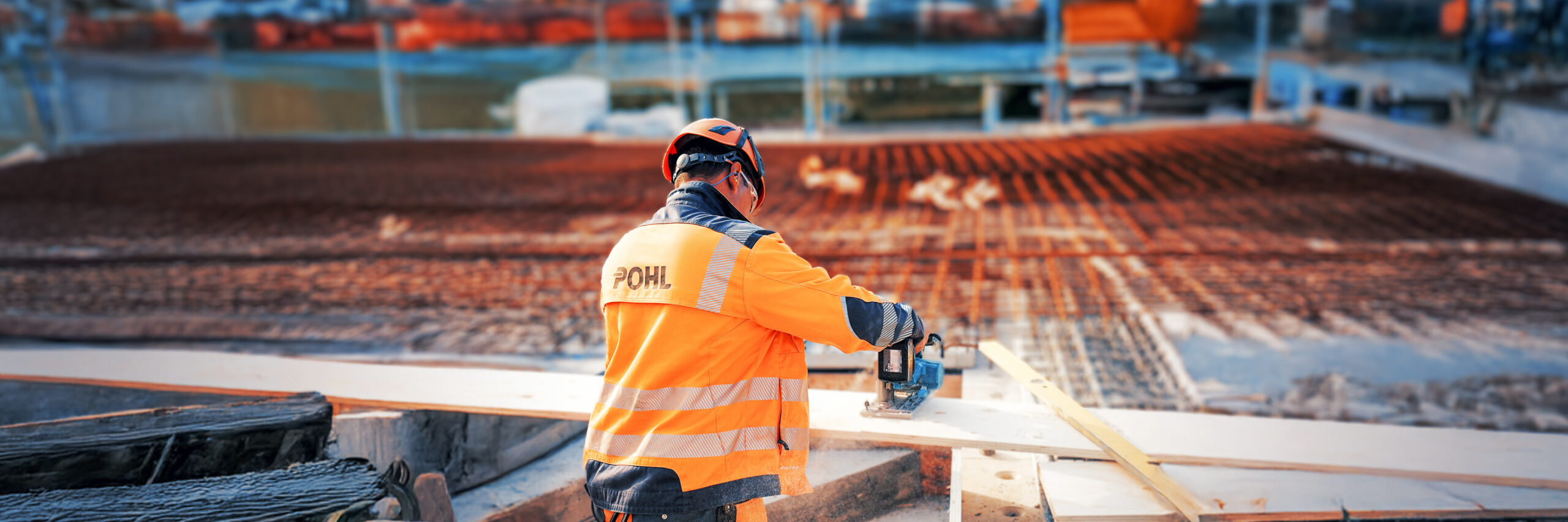 Mitarbeiter von POHL in orangener Schutzkleidung arbeitet mit Elektrosäge an einer Holzplatte.
