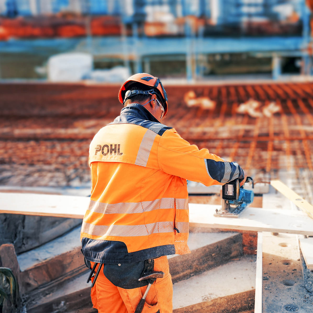 Mitarbeiter von POHL in orangener Schutzkleidung arbeitet mit Elektrosäge an einer Holzplatte.