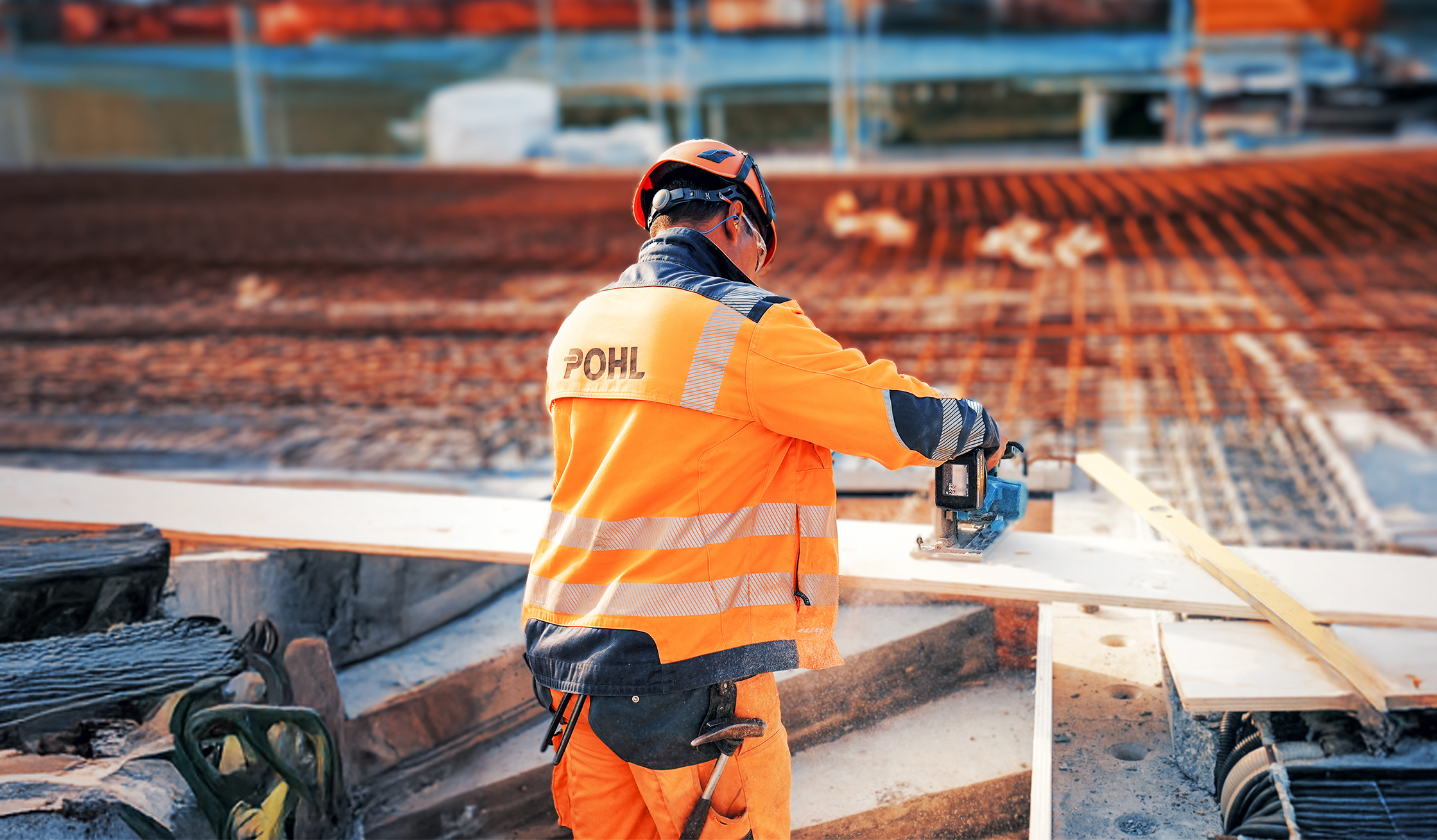 Mitarbeiter von POHL in orangener Schutzkleidung arbeitet mit Elektrosäge an einer Holzplatte.