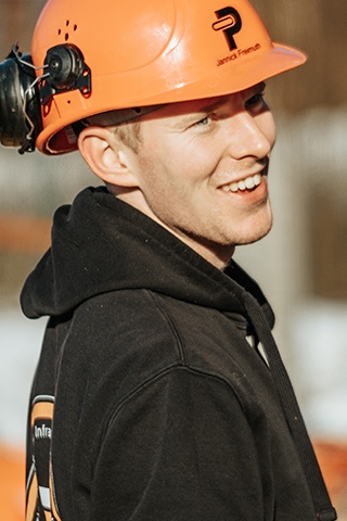 In der Mitte ist der Kopf eines POHL-Mitarbeiters mit orangefarbenem Helm im Profil zu sehen; links am Helm ist Gehörschutz befestigt, im Hintergrund ist alles unscharf.