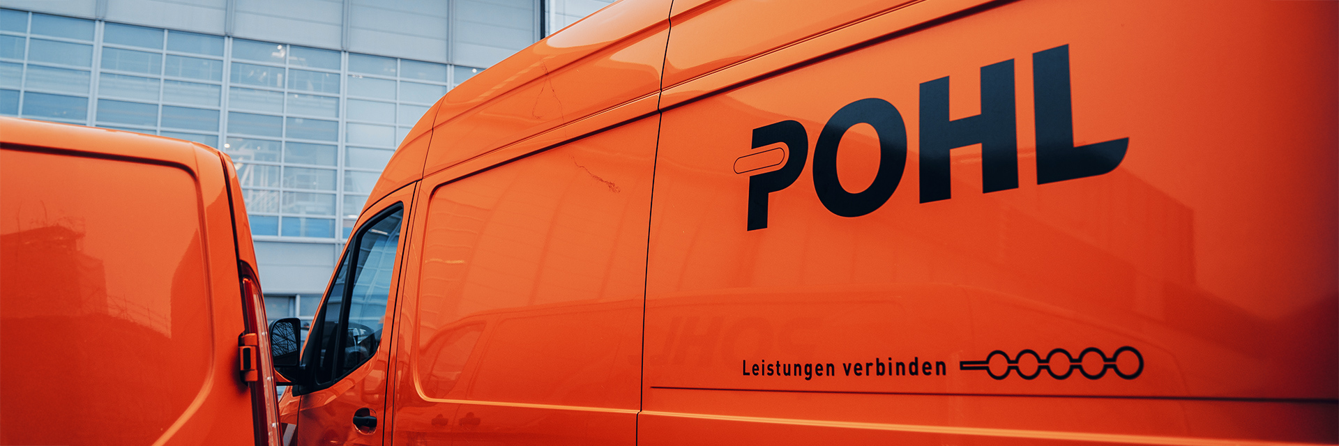 Standort Hamburg Finkenwerder: Vorne im Bild füllt die Seitenwand eines POHL-Fahrzeugs in Orange den rechten Bildteil; darauf steht groß „POHL“ und darunter „Leistungen verbinden“. Links am Rand steht ein weiteres orangefarbenes Fahrzeug. Im Hintergrund ist die Glasfassade eines großen Gebäudes.Vorne im Bild füllt die Seitenwand eines POHL-Fahrzeugs in Orange den rechten Bildteil; darauf steht groß „POHL“ und darunter „Leistungen verbinden“. Links am Rand steht ein weiteres orangefarbenes Fahrzeug. Im Hintergrund ist die Glasfassade eines großen Gebäudes.
