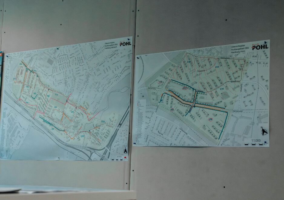 Zwei großformatige technische Karten hängen nebeneinander an einer grauen Wand. Die Pläne zeigen Straßennetze und markierte Leitungs- oder Bauabschnitte, beschriftet mit dem POHL-Logo.