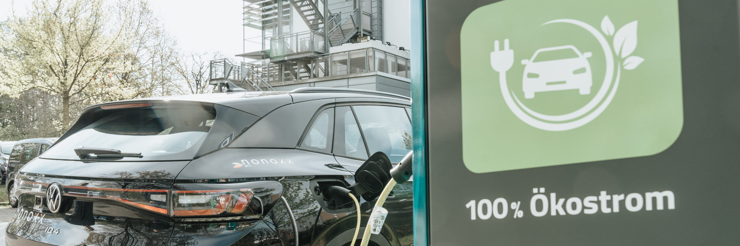 Umweltmanagement: Ladesäule für Elektroautos mit Ökostrom Schriftzug, links daneben ein E-Auto mit eingestecktem Ladekabel.