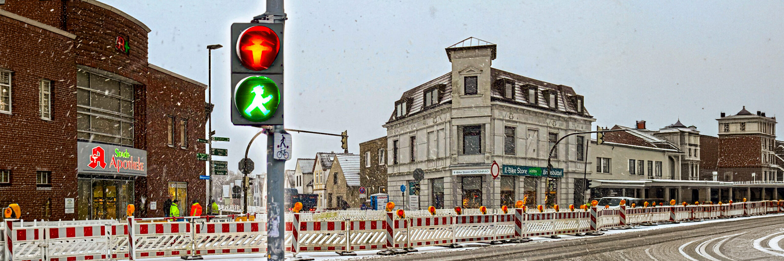 Winterliche Straßenszene mit Fußgängerampel (rot/grün) in Brunsbüttel. Zu sehen ist ein Baustelle mit Absperrungen. Im Hintergrund sind ein paar Geschäfte.
