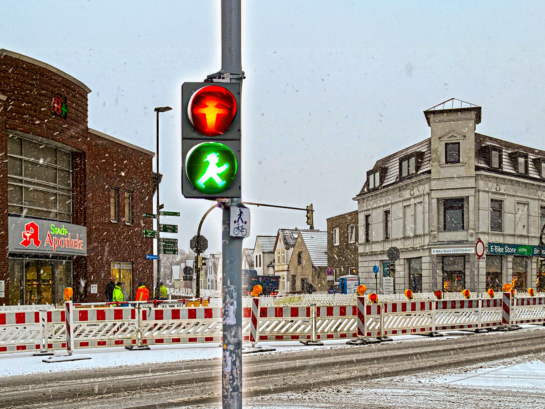 Winterliche Straßenszene mit Fußgängerampel (rot/grün) in Brunsbüttel. Zu sehen ist ein Baustelle mit Absperrungen. Im Hintergrund sind ein paar Geschäfte.