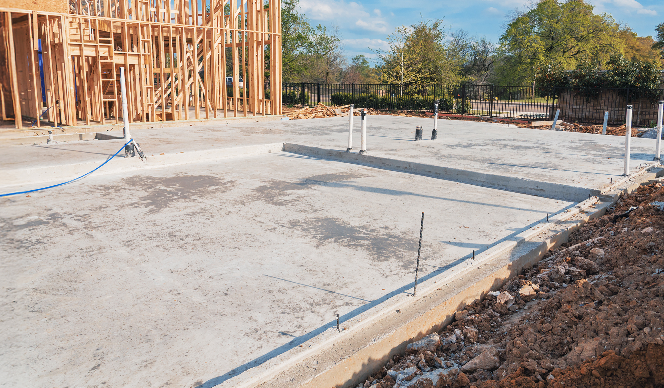 Betonfundament mit sichtbaren Leitungen und Holzrahmenkonstruktion im Hintergrund.