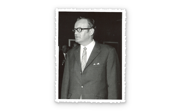 Schwarzweißporträt eines Mannes im Anzug mit Brille und Krawatte, er blickt leicht nach rechts.