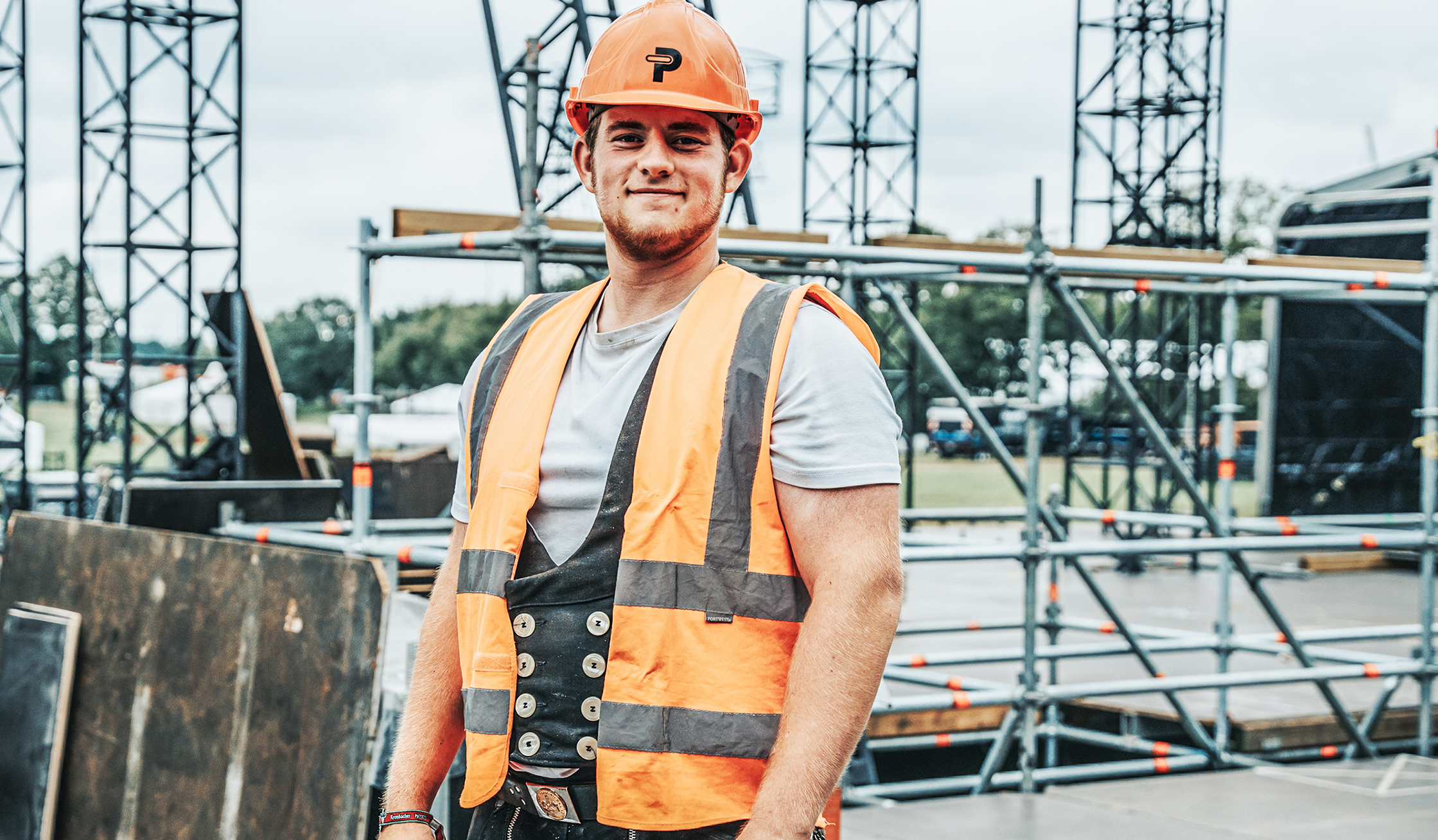 In der Mitte steht ein POHL-Mitarbeiter mit orange Helm und Warnweste vor Gerüsttürmen. Links und rechts ziehen sich Metallgerüste über den Platz; der Boden ist mit Platten ausgelegt.